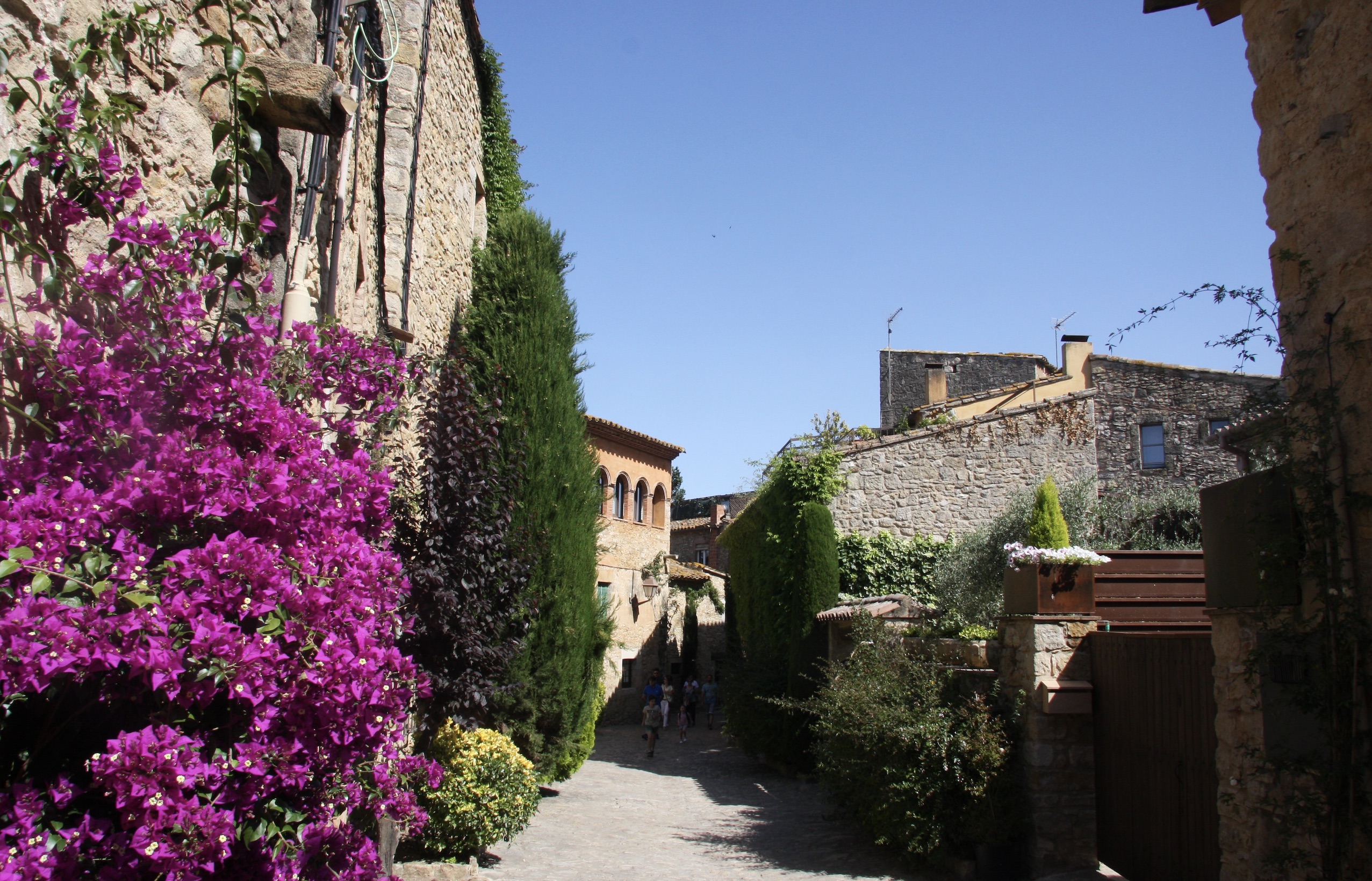 Sunny street in Peratallada village with trees and flowers